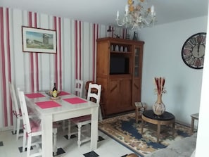 Zona pranzo con tavolo bianco, sedie, un mobile in legno, una sveglia e un lampadario.