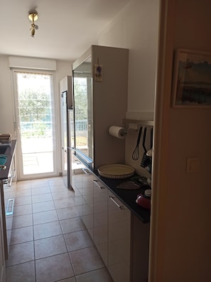 A kitchen with a refrigerator, a sink, and a window. - 2-room apartment, 45 m², ground floor, garden 50 m² + terrace 26 m² (Hyères)