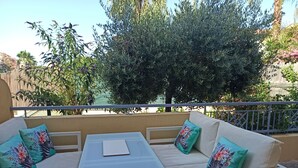 A balcony with a white sofa, a small table, and a view of greenery and a building. - 2-room apartment, 45 m², ground floor, garden 50 m² + terrace 26 m² (Hyères)
