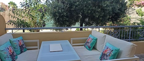A balcony with a white sofa, a small table, and a view of greenery and a building.