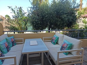 A balcony with a white sofa, a small table, and a view of greenery and a building. - 2-room apartment, 45 m², ground floor, garden 50 m² + terrace 26 m² (Hyères)