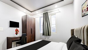 Een hotelkamer met een bed, een bureau, een stoel, een kast, een televisie, een raam met gordijnen en een schilderij aan de muur.