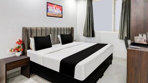 Een hotelkamer met een bed, een nachtkastje met een bloevas, een schilderij aan de muur, een raam met gordijnen en een houten kast.