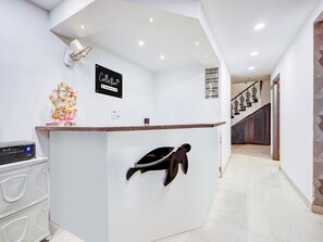 A reception desk with a sign reading 'Collection,' a statue of a deity, a coat rack, and a staircase in the background. - Super Collection O Shalimar Bagh (New Delhi)