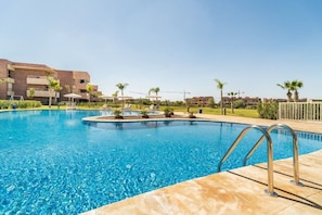 Una piscina con agua cristalina y azul, rodeada por una terraza con baldosas y algunas sillas de descanso.