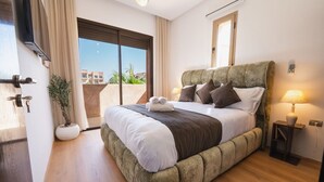 A bedroom with a large bed, a potted plant, a sliding door to a balcony, and a bedside table with a lamp. - Prestigia Golf Resort |Luxury 3BR| Pool&Atlas View (Marrakesh)