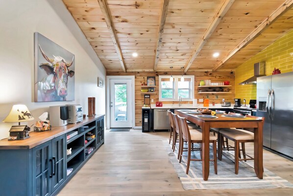 Eine moderne Küche mit Holzbalkendecke, einem Essbereich mit Holztisch und -stühlen sowie einer Kücheninsel mit Spüle und Geräten.