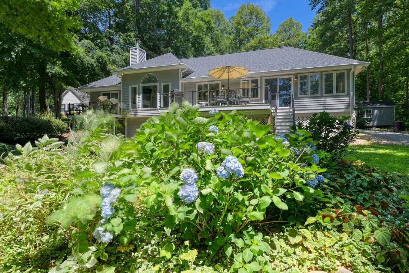 Une maison à deux étages dotée d’un porche abrité, entourée d’une végétation luxuriante et de buissons d’hortensias.