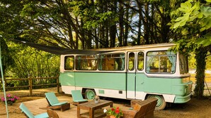 Un autobus d’époque transformé en espace de vie fixe, doté d’une terrasse, de chaises longues et d’une table.
