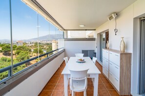 Ein Balkon mit weißem Tisch und Stühlen, einer Vase und Blick auf eine Stadtlandschaft.