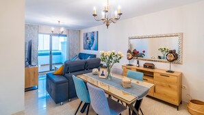 Un salon moderne comprenant un canapé, une table à manger, des chaises, un lustre et un grand miroir.