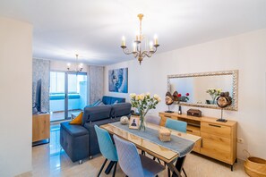 A modern living room with a sofa, dining table, chairs, a chandelier, and a large mirror. - Cubo's Vega Fuengirola Apartment & Parking / communal pool / terrace / free wifi (Fuengirola)