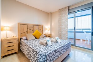 Ein Hotelzimmer mit einem Bett, zwei Nachttischen, einem kleinen Tisch, einem Balkon mit einem Stuhl und Blick ins Freie.