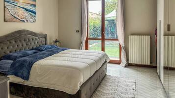 A bedroom with a bed, a radiator, a window with curtains, and a painting on the wall.