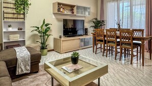Een woonkamer met een bank, salontafel, televisie, boekenkast en een eethoek.