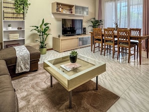 A living room with a sofa, coffee table, TV, bookshelf, and dining area. - Villa Garden (Porto San Giorgio)