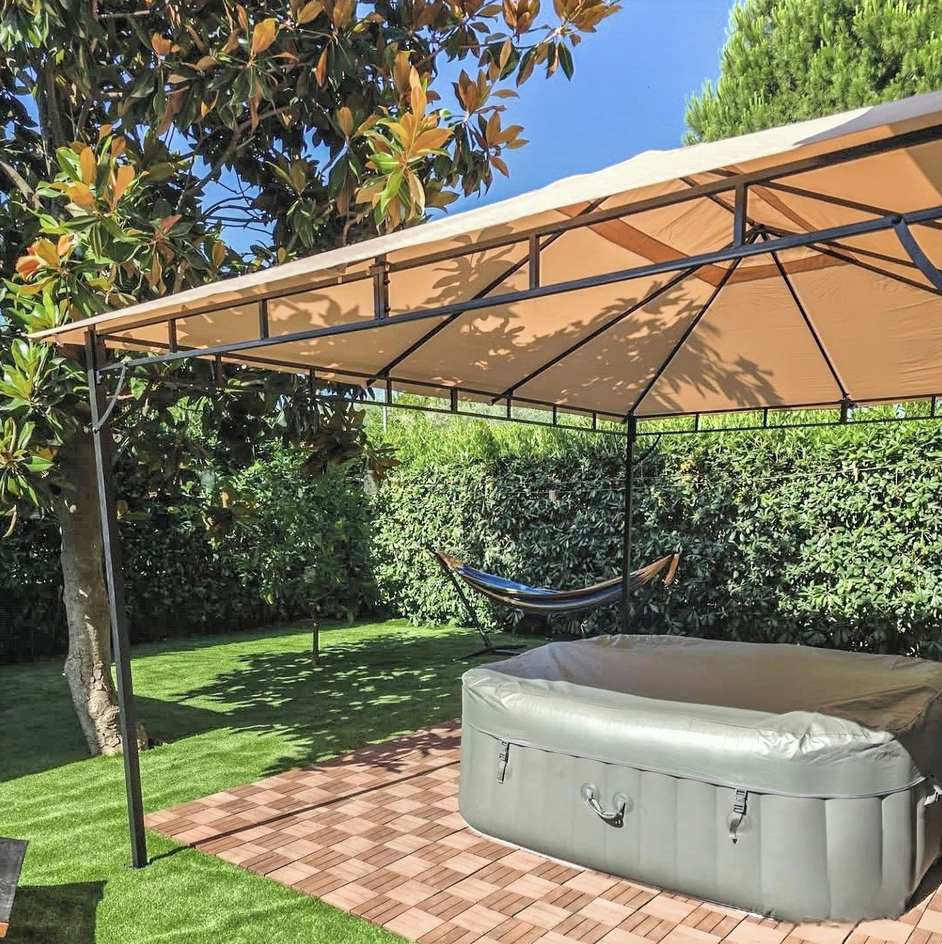 Un espace extérieur abrité comprenant un hamac, un grand matelas gonflable et un arbre.