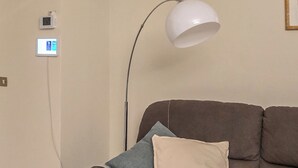 A brown sofa with two pillows, a white floor lamp, a glass table with a potted plant, and a framed picture on the wall.