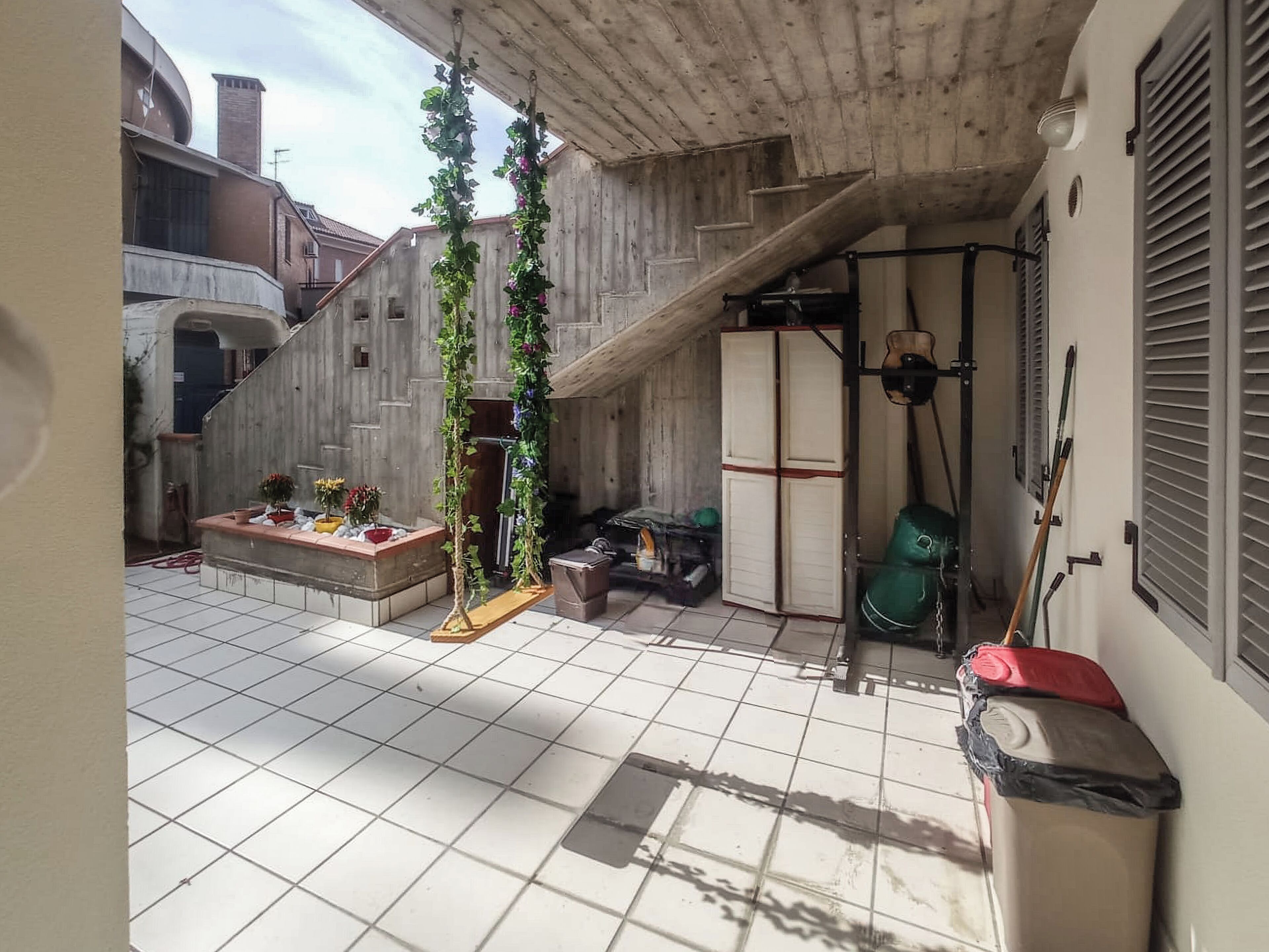 Une terrasse carrelée avec un escalier en bois, une petite table décorée de fleurs, un sac vert et un sac rouge.