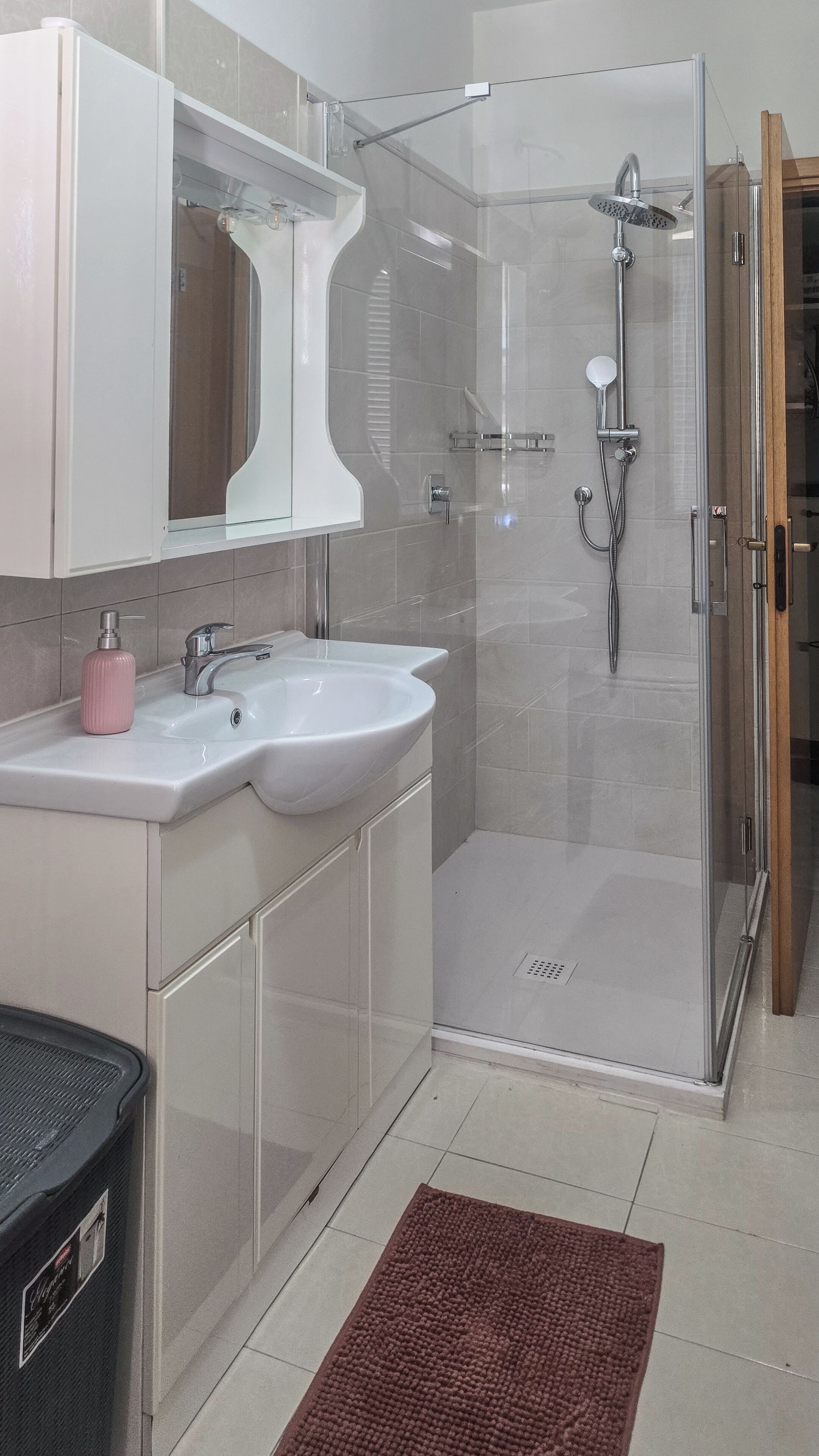 Ein modernes Badezimmer mit einer Duschkabine, zwei Waschbecken und einem großen Spiegel über dem Waschtisch.