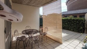 A covered patio with a table and chairs, a woven screen, and a tiled floor.