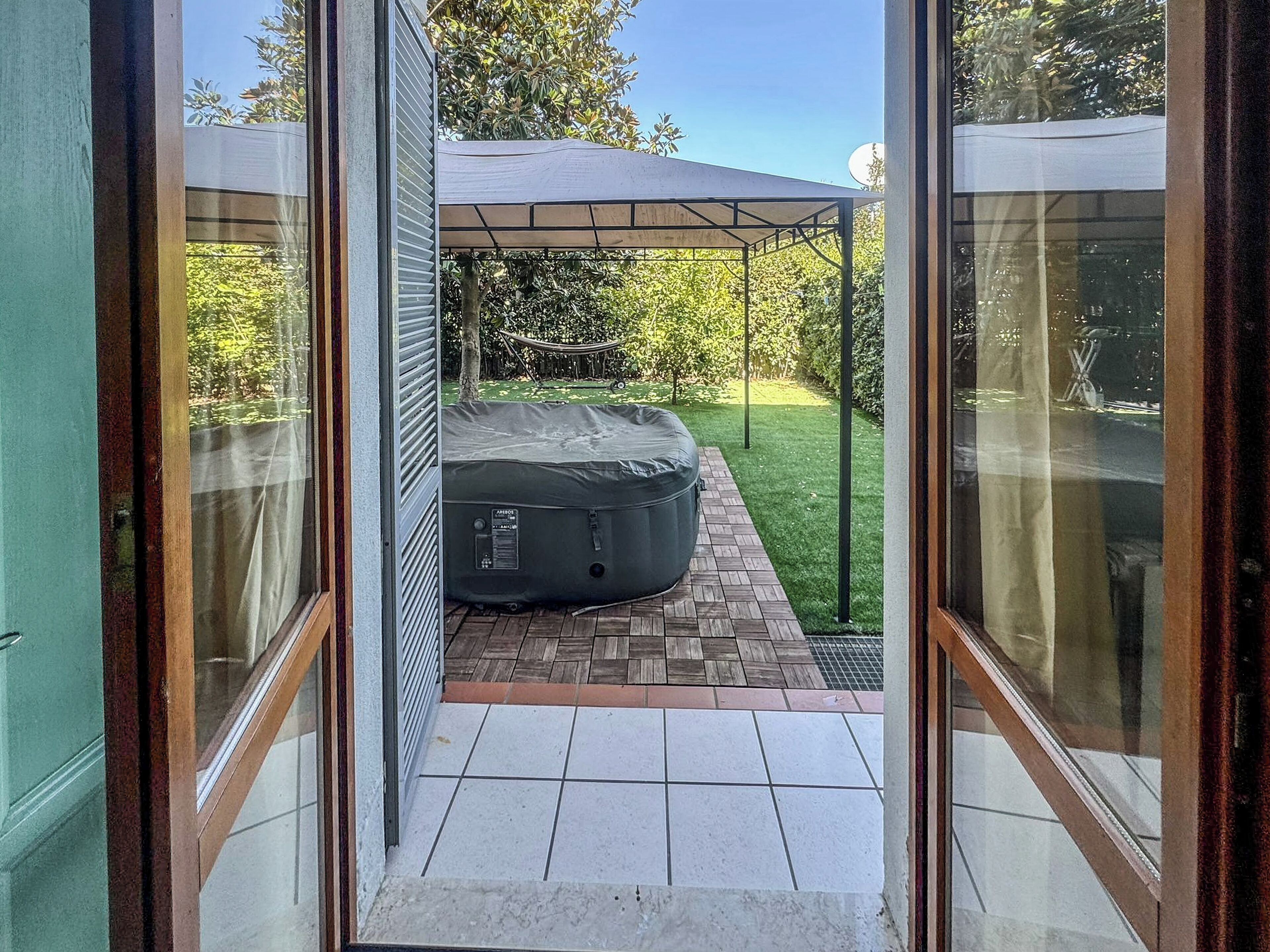 Un patio con hidromasaje, un área de estar techada y un césped bien cuidado.