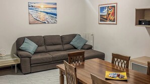 A dining area with a wooden table and chairs, a sofa with cushions, and two wall-mounted paintings.