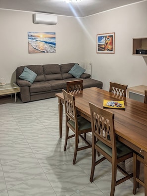 Ein Essbereich mit Holztisch und Stühlen, einer Couch mit Kissen sowie zwei an der Wand hängenden Bildern.
