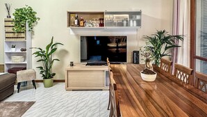 Een moderne woonkamer met een houten eettafel, een televisie en verschillende planten.