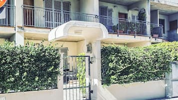 A multi-story residential building with balconies, a gated entrance, and a clear sky.