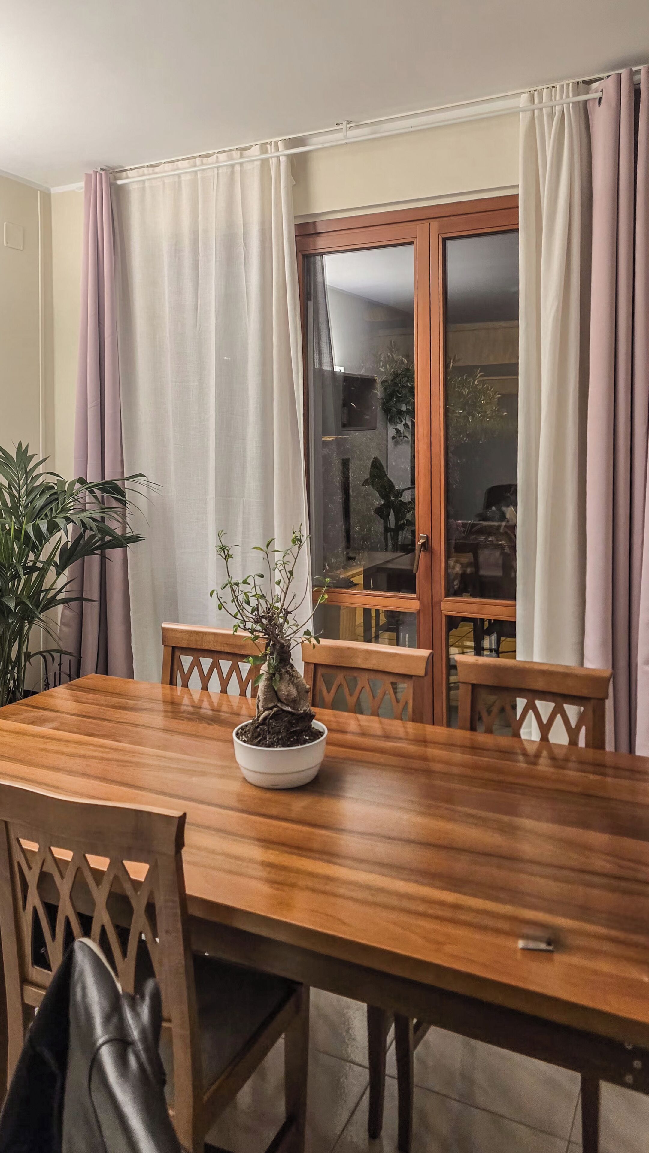 Un coin repas avec une table en bois, des chaises, une plante en pot et une porte-fenêtre à glissière avec des rideaux.