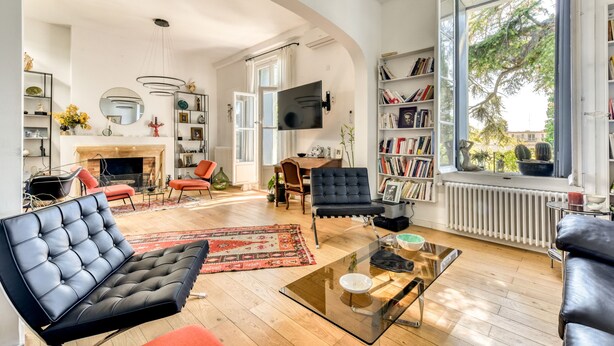 Ein modernes Wohnzimmer mit Kamin, Bücherregalen, einem Flachbildfernseher und einem großen Fenster mit Blick auf Bäume.