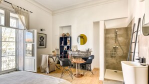 Ein Schlafzimmer mit Bett, Schreibtisch mit Schachbrett, Badezimmer mit Dusche und Blick ins Freie.