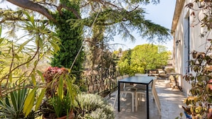 Eine Terrasse im Freien mit Tisch und Stühlen, umgeben von Kübelpflanzen und Bäumen.