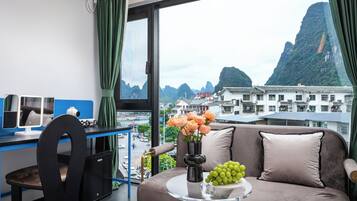 Habitación con vista a las montañas, un sofá, un escritorio con computadora y un florero con flores.