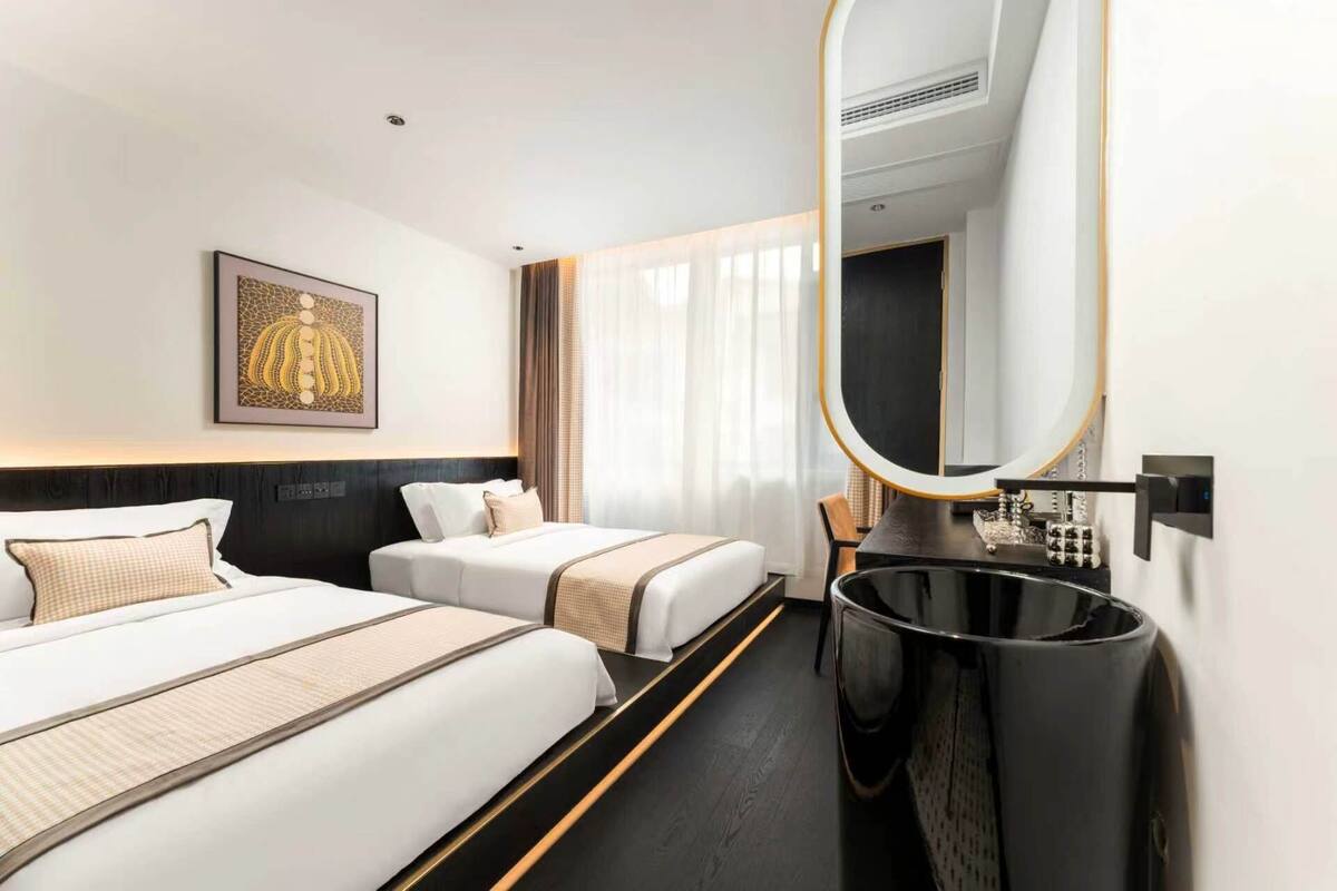 A hotel room with two beds, a large mirror, a framed artwork, and a modern bathroom.
