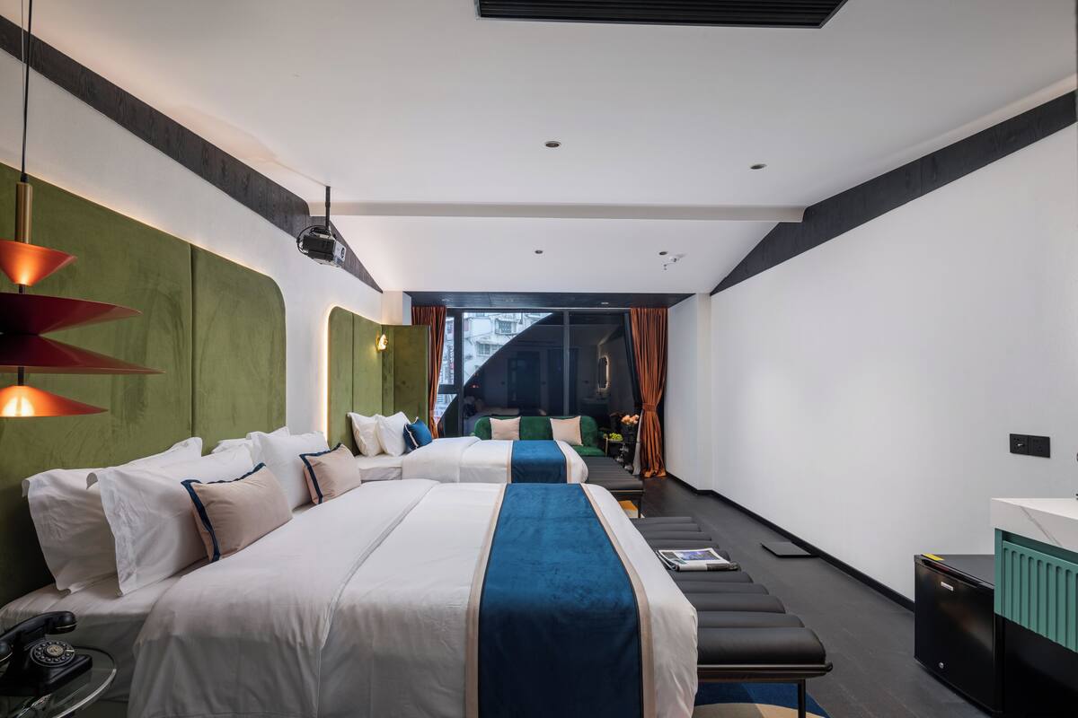 A modern hotel room with two beds, a desk, a telephone, and a view of the city.