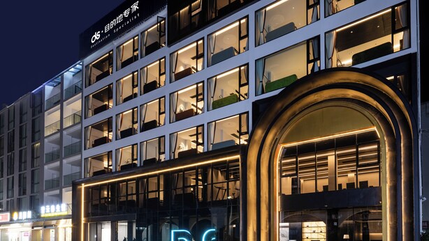 A multi-story hotel with a prominent neon sign, large windows, and a reflective entrance area.