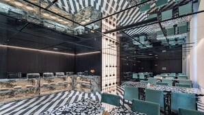A modern restaurant with marble countertops, green upholstered chairs, and a patterned floor.