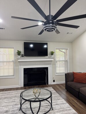 A living room with a fireplace, a ceiling fan, a flat-screen TV, and a sofa.