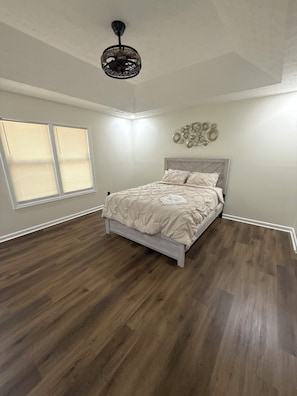 Ein Schlafzimmer mit einem Bett, einem Deckenventilator, einem Fenster mit Jalousien und einer Wandleuchte.
