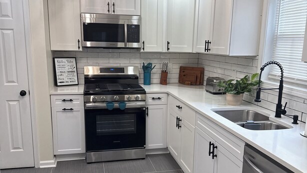 Una cocina moderna con armarios blancos, electrodomésticos de acero inoxidable y piso de baldosas.