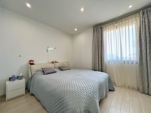 Ein Schlafzimmer mit Bett, Nachttisch, Lampe und Vorhängen.
