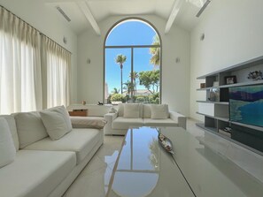 A modern living room with a large arched window, a white sofa, a coffee table, and a TV on a stand.