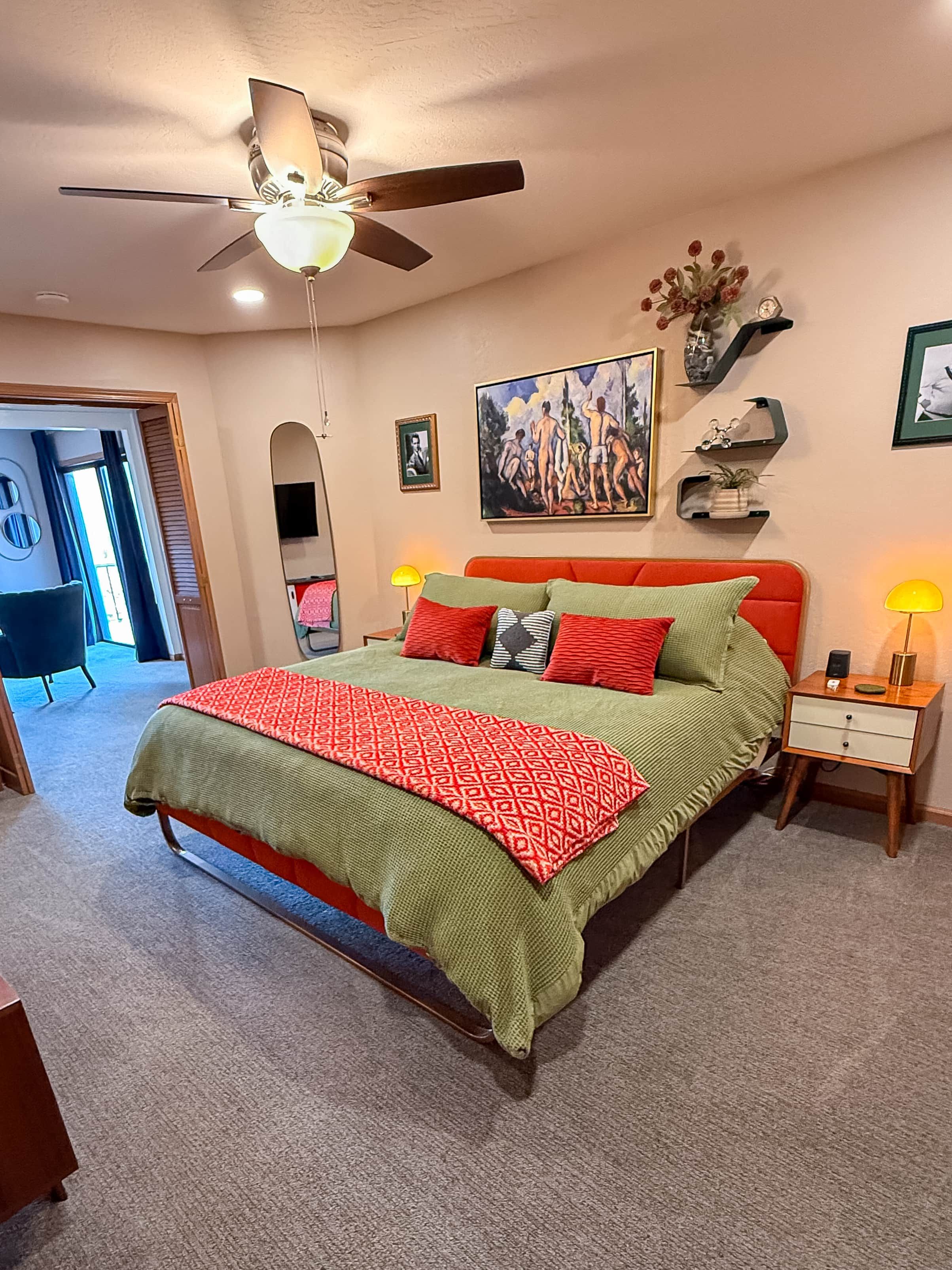 A bedroom with a bed, a ceiling fan, a nightstand, a lamp, and a painting on the wall.