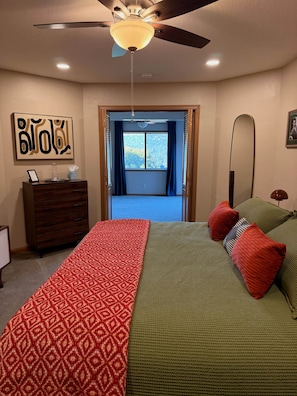 A bedroom with a bed, a dresser, a ceiling fan, a window with curtains, and a wall-mounted mirror.