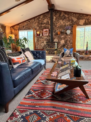 A cozy living room with a stone wall, a fireplace, a blue sofa, a patterned rug, and a coffee table with books and a plant.