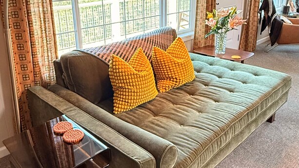 Ein Sofa mit einer gepolsterten Oberfläche, ein Beistelltisch, eine Stehlampe und Blick durch große Fenster.