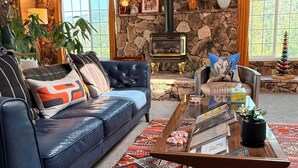 A cozy living room with a stone wall, a fireplace, a blue sofa, a patterned rug, and a coffee table with books and a plant.