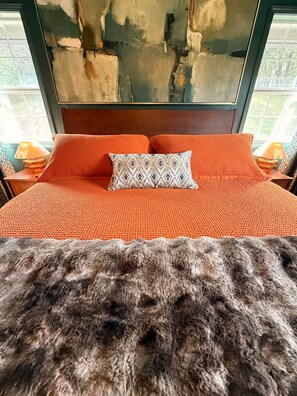 A bed with an orange textured bedspread and a patterned pillow, a wooden headboard, and a view of the outdoors through a window. - Brando King Room at Mountain Daddies B & B (Oakhurst)
